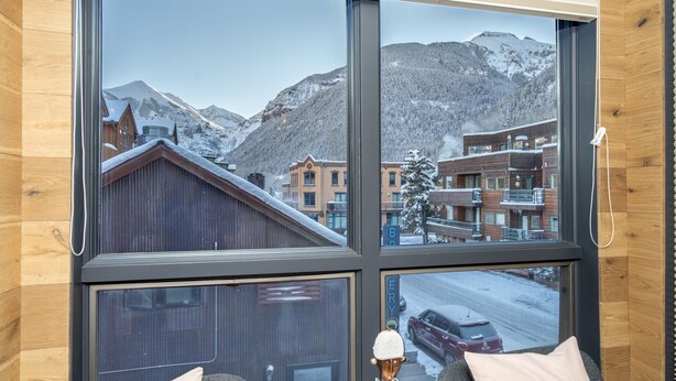 A room with large windows offering a view of a snowy mountain and buildings. - One block walk to gondola, ski lockers downstairs, River Trail close by! (Telluride)
