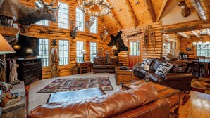 A log cabin interior with wooden walls, a fireplace, leather furniture, and mounted animal heads. - Mountain Escape w/ Fire Pit, Pool Table & Hot Tub! (OAKLAND)