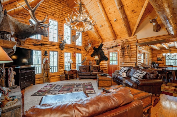 A log cabin interior with wooden walls, a fireplace, leather furniture, and mounted animal heads.