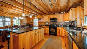 A spacious kitchen with wooden cabinets, a large island, and a black stove. - Mountain Escape w/ Fire Pit, Pool Table & Hot Tub! (OAKLAND)