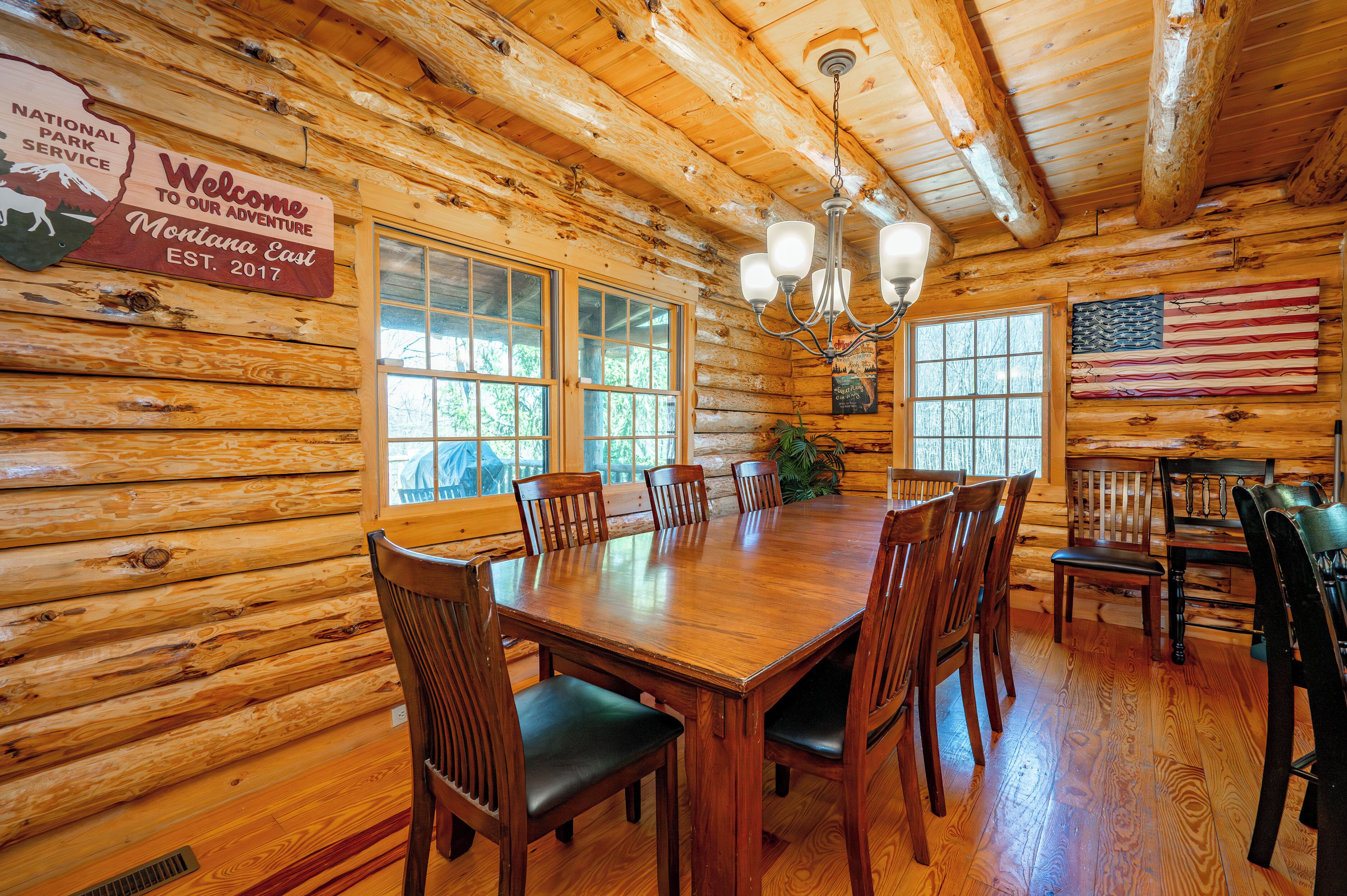 A wooden cabin interior with a large dining table, chairs, a chandelier, and an American flag.