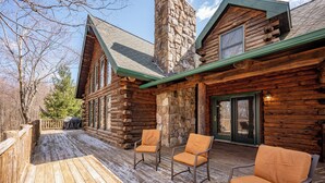 A log cabin with a wooden deck, two chairs, and a stone chimney. - Mountain Escape w/ Fire Pit, Pool Table & Hot Tub! (OAKLAND)