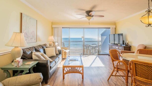 Een ruime woonkamer met een bank, stoelen, een salontafel en een balkon met uitzicht op de oceaan.