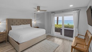 A bedroom with a large bed, a ceiling fan, a nightstand with a lamp, a chair, and a view of the ocean through a sliding door. - Gulf-Front, Remodeled Unit w/ Incredible Views + Free Attraction Tickets! (Seacrest)