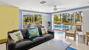 Un salon moderne avec un canapé en cuir noir, un coin repas avec des sièges extérieurs et une vue sur une piscine.