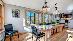 A spacious dining area with a long wooden table, multiple chairs, and large windows offering a view of the outdoors. - Beautiful new 4 bed/4bath private home, 4 blocks off Main St with all the amenities!! (Frisco)