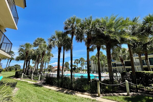 A pool area with palm trees and a clear blue sky. - FREE DAILY ACTIVITIES and listen to the sounds of the ocean from this gorgeous sunlit upgraded unit! (Saint Augustine)