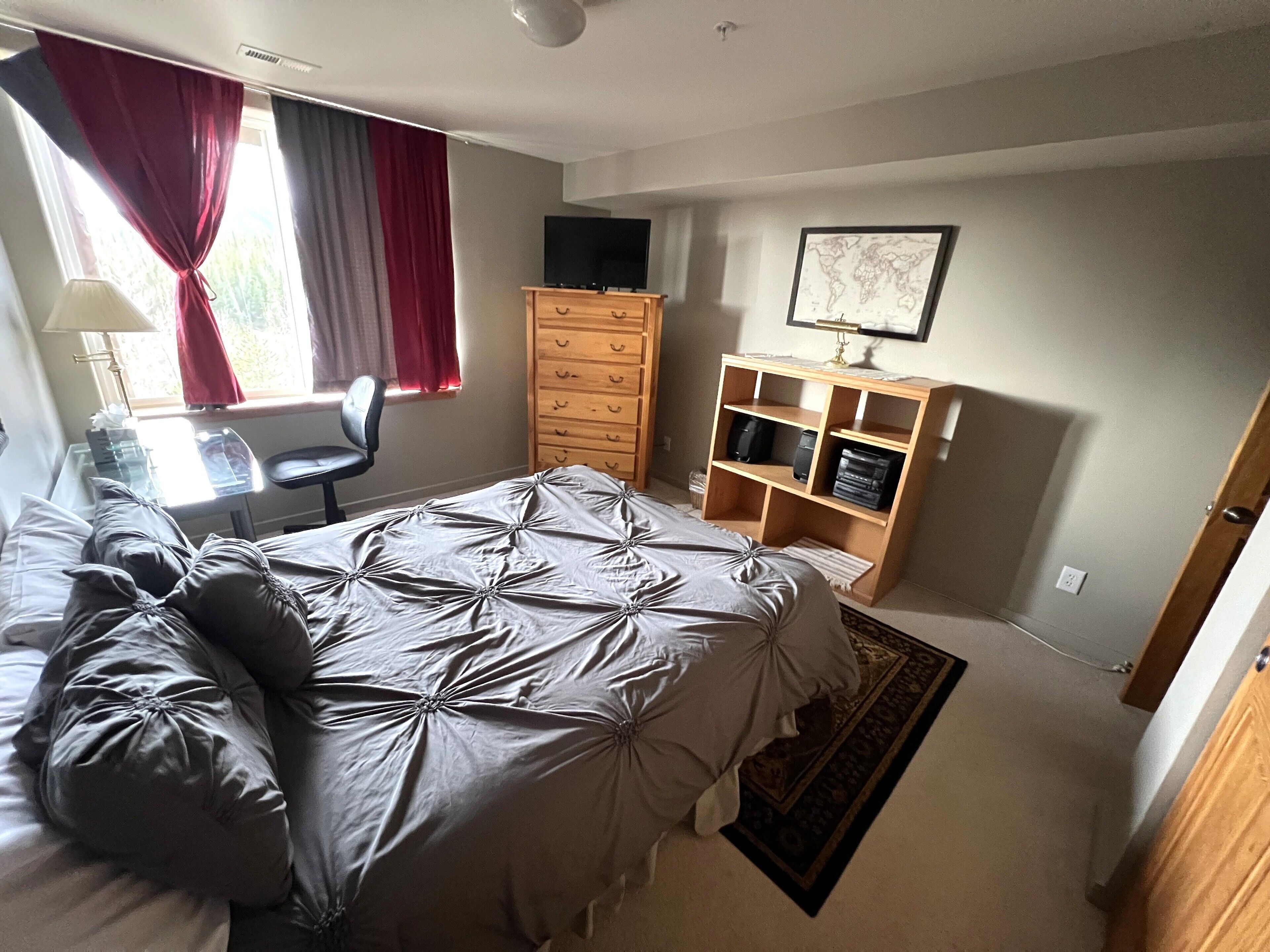 Un dormitorio con cama, escritorio, silla, cómoda y televisor.