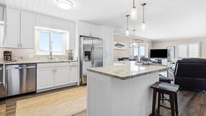 A modern kitchen with white cabinetry, stainless steel appliances, a large island, and pendant lighting.