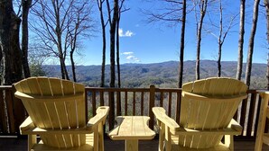 A wooden deck with two Adirondack chairs and a small table, overlooking a mountainous landscape. - Sunset Ridge - New Hot Tub! Log Cabin, Views, Deck, Trails (Ferguson)