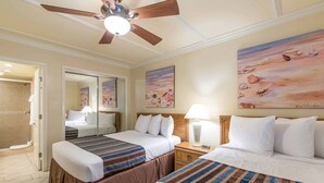Habitación de hotel con dos camas, ventilador de techo y obras de arte en las paredes.