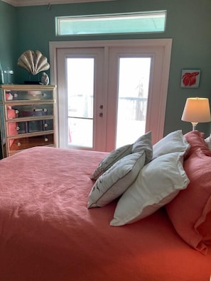 Ein Schlafzimmer mit einem Bett, einem Schminktisch, einer Lampe und Blick durch eine Tür.