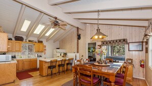 A spacious kitchen with wooden cabinets, a central island, and a ceiling fan. - Whispering Bear Lodge by Destination Big Bear : Pool Table! Foosball! Views! Internet! Deck! (Big Bear City)