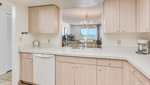 A modern kitchen with light wood cabinets, a central island with a sink, and a view to the dining area.