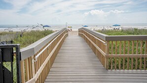 A wooden boardwalk leading to a beach with a fence on one side and a grassy area on the other. - Florence I 706 - Bargain beachfront vacay;Shining pool;Prime locale (South Padre Island)