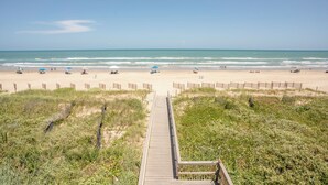 A beach with a wooden boardwalk leading to the shore, surrounded by grassy dunes and a wooden fence. - Florence I 706 - Bargain beachfront vacay;Shining pool;Prime locale (South Padre Island)