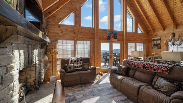 A spacious log cabin interior with a stone fireplace, large windows, and a cozy seating area.