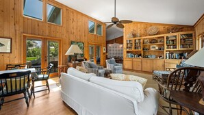 A spacious living room with a high ceiling, wooden walls, and a large bookshelf filled with books and decorative items. - Natural and Serene Home Away from Home (Georgetown)