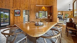 A wooden-paneled dining area with a large table and chairs, a kitchen in the background, and a view of the outdoors. - Natural and Serene Home Away from Home (Georgetown)