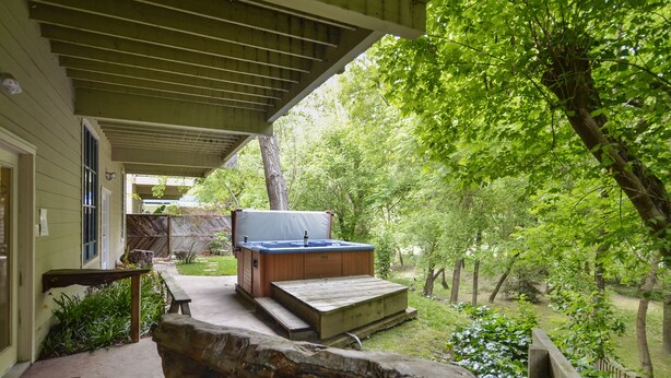 Un'area esterna coperta con vasca idromassaggio, terrazza in legno e elemento decorativo in pietra.