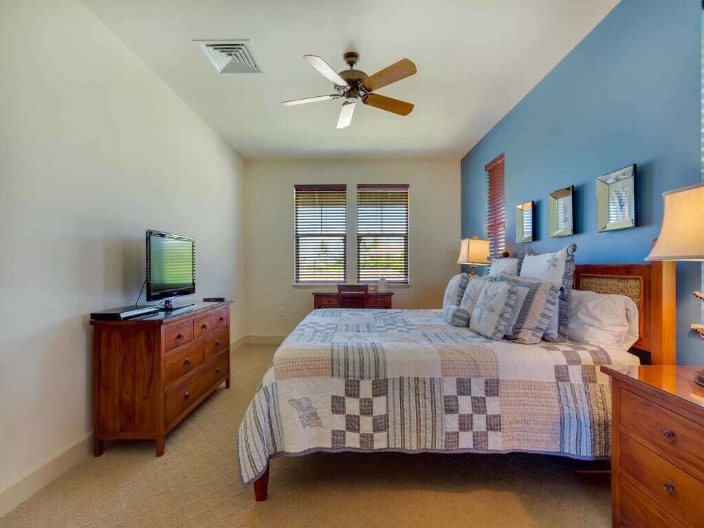 A bedroom with a bed, a ceiling fan, a television on a dresser, and a window with blinds.
