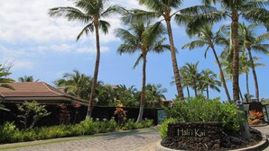 A tropical resort entrance with palm trees, a stone pathway, and a sign reading "Hali'i Kai".