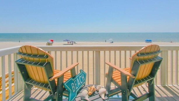 A deck with two Adirondack chairs facing a beach. A sign on the deck reads "BEACH."