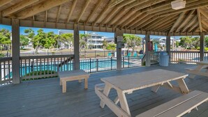 A covered outdoor area with picnic tables and a pool in the background.