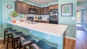 A modern kitchen with dark wooden cabinets, a large island with bar stools, stainless steel appliances, and teal walls.