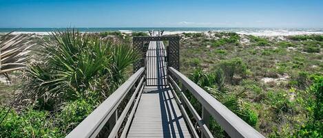 Un paseo marítimo de madera que lleva a una playa, con vista despejada al océano.