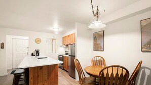 Uma cozinha com armários de madeira, bancada branca e área de refeições com mesa e cadeiras de madeira.