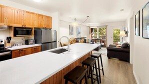 Uma cozinha moderna com armários de madeira, uma ilha grande, eletrodomésticos de aço inoxidável e uma área de refeições com sofá e mesa.