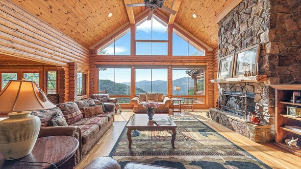 L’intérieur d’une cabane en rondins, avec une cheminée en pierre, de grandes fenêtres et un coin salon confortable.