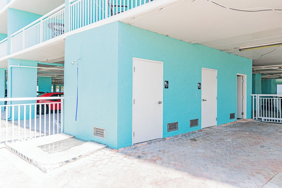 A building with a light blue exterior, white doors, and a covered parking area.