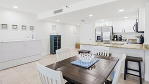 Une cuisine moderne avec des meubles blancs, une table à manger avec des chaises et un îlot de cuisine équipé d’un réfrigérateur et d’une machine à café.