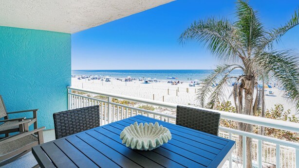 Un balcon donnant sur la plage, une table agrémentée d’un vase décoratif et une chaise.