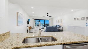 Une cuisine moderne dotée de plans de travail en granit, d’un évier double et offrant une vue sur l’espace de vie.
