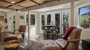 Un salón amplio con sillones de cuero, una mesa de centro y un televisor. Hay ventanas grandes y un balcón con mobiliario exterior.