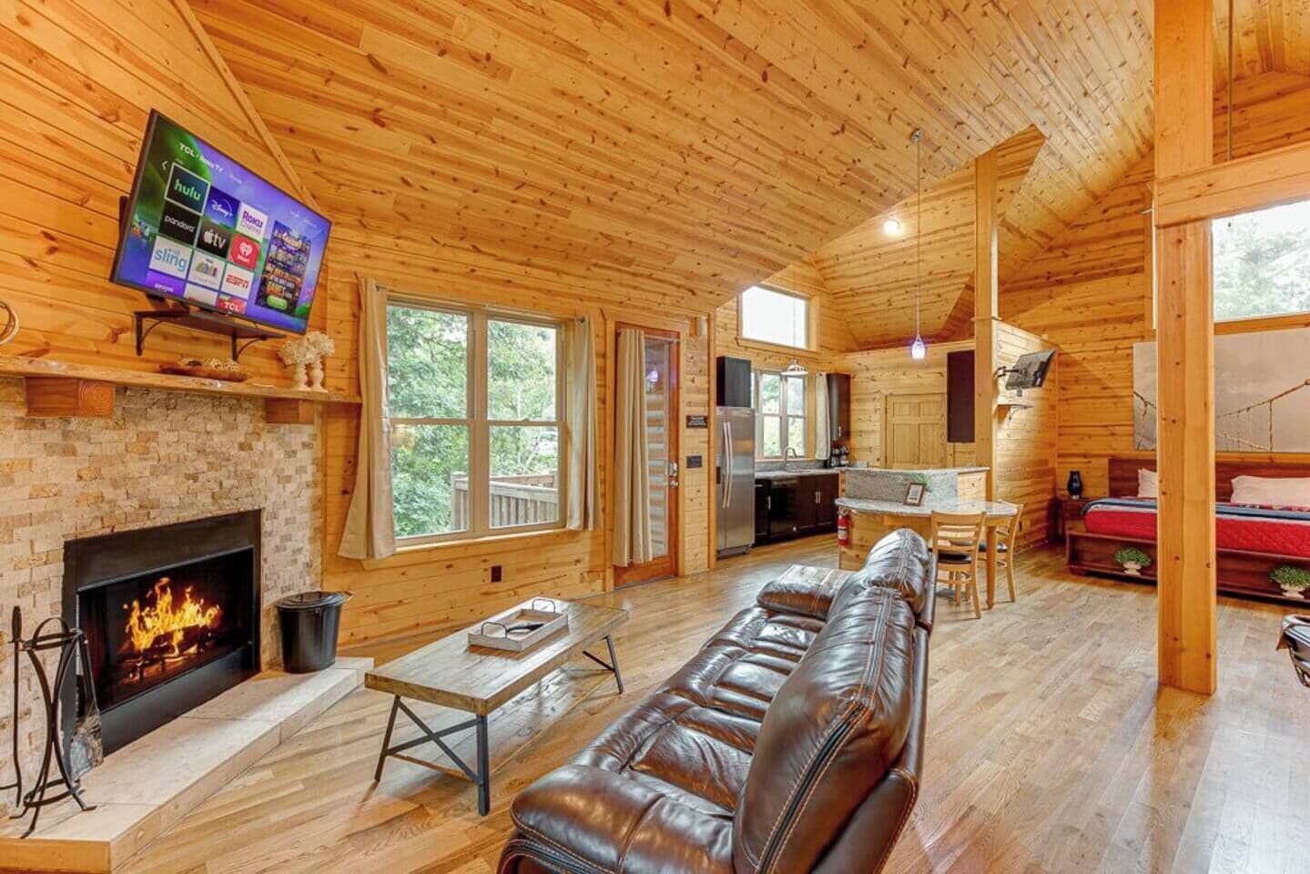 A log cabin interior with a fireplace, leather sofa, wooden floors, and a TV displaying streaming services.