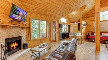 A log cabin interior with a fireplace, leather sofa, wooden floors, and a TV displaying streaming services.