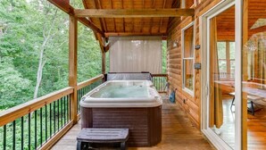 Een houten hut met een hottub op een balkon, omringd door bomen.