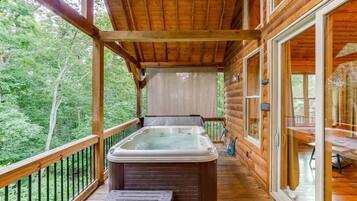 Una cabaña de madera con un jacuzzi en el balcón, rodeada de árboles.