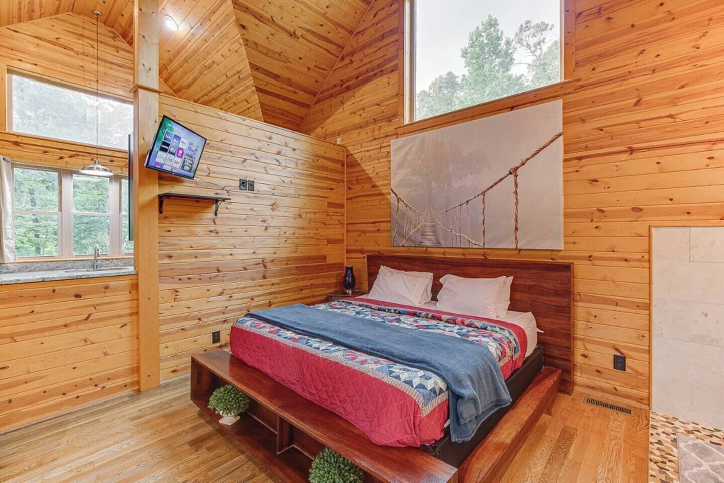 Une chambre dans une cabane en bois, avec un lit, une télévision et une grande fenêtre.