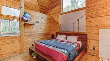 Une chambre dans une cabane en bois, avec un lit, une télévision et une grande fenêtre.