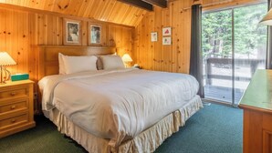 A wooden room with a bed, two bedside tables, and a window with a view of trees.