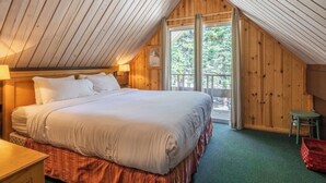 A bedroom with a large bed, wooden walls, a balcony, and a small table.
