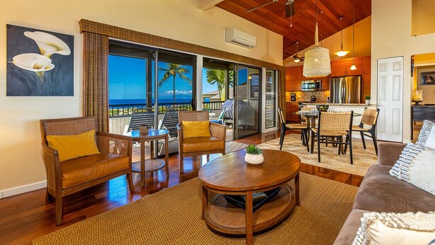 A spacious living area with a wooden ceiling, a large window with a view of the ocean, and a kitchen with modern appliances.
