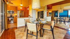 A spacious kitchen with modern appliances, a dining area with wicker chairs, and a view of the ocean.