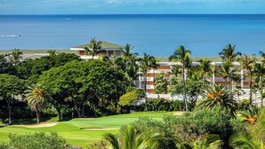 A golf course with a view of the ocean and a hotel with multiple floors and palm trees.
