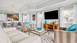 A modern living room with a sofa, armchairs, a glass coffee table, a TV, and a kitchen in the background. - Condo with Golf Course Views, Near Attractions (Kissimmee Fl)